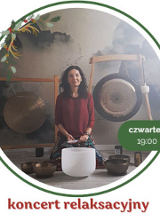 Kobietę ubrana w bordową bluzkę siedzi przed dużym gongiem oraz kilkoma złotymi misami. Kobieta ma ciemne włosy i patrzy w obiektyw aparatu, lekko się uśmiecha.