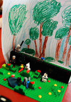 Na zdjęciu znajduje się budowla lego, sześć figurek ustawionych na zielonych podstawkach najprawdopodobniej imitują walkę.