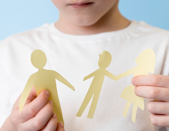 Zdjęcie przedstawia dziecko trzymające wycinankę w kształcie ludzi - dorosłego i dwóch dzieci, próbuje je połączyć