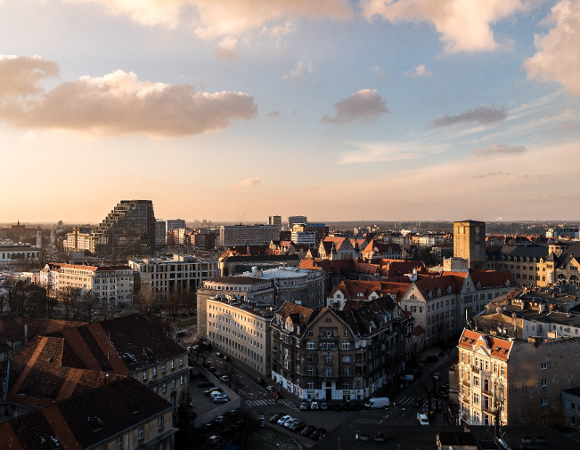 Zdjęcie przedstawia widok z lotu ptaka na centrum Poznania, nad którym zachodzi słońce.