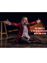 zdjęcie przedstawia aktora siedzącego na scenie, ubranego w wiśniową brokatową marynarkę, koszulę w błękitne pionowe paski oraz ciemne spodnie. Ręce ma rozłożone. Patrzy na widownię. Za aktorem po lewej stronie stoi wysoki stołek, a po prawej leży kontrabas.