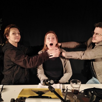 Na zdjęciu trzy osoby, dwie trzymają za szyję osobę w środku, dusząc ją.