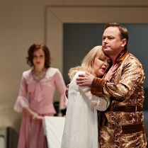 Na pierwszym planie obejmująca się para - kobieta w koszuli nocnej, mężczyzna w szlafroku. W tle kobieta w rózowej sukience, która na nich patrzy.