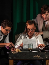 Trzech mężczyzn, jeden z nich siedzi przy stole i pisze coś na maszynie do pisania, Dwóch pozostałych stoi obok niego - jeden z nich trzyma ręce na barkach piszącego.