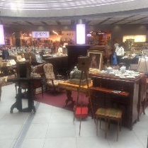 Różne przedmioty, w tym krzesła, stoły, stojaki oraz drewniane pianino w galerii handlowej.