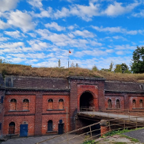 Zdjęcie wejścia do ceglanego fortu, na którego dachu rośnie trawa i drzewa.