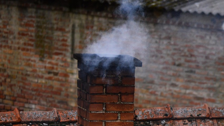 Ilustracja przedstawia stary komin z cegły na dachu, z którego leci dym.