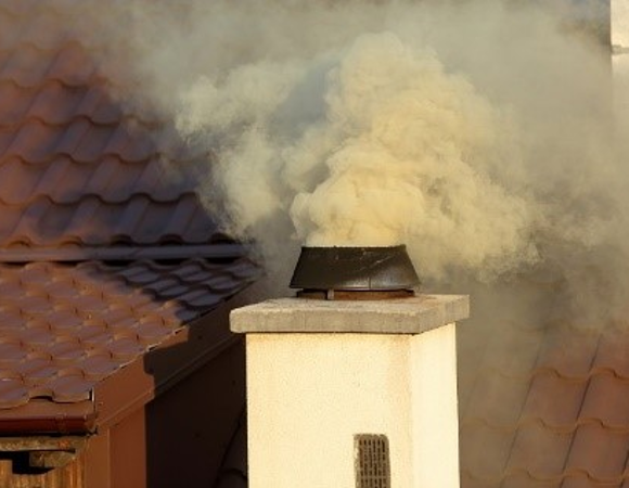 Zdjęcie przedstawia komin, z któego wydobywają się żółto-białe kłęby dymu.