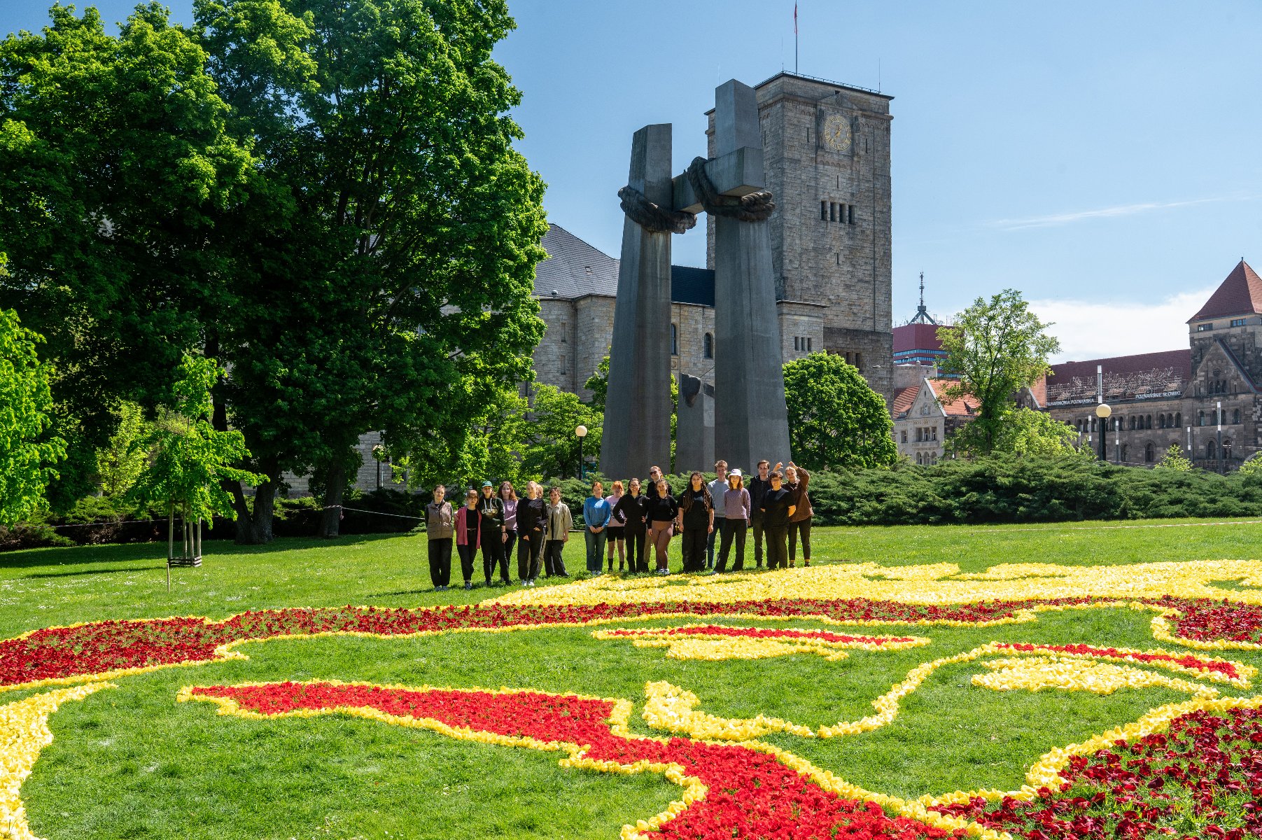 Nad kompozycją kwietną pracują studenci z Koła Naukowego Architektury Krajobrazu Uniwersytetu Przyrodniczego Zdjęcie przedstawia młodych ludzi układających kompozycję z kwiatów.