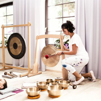 Kobieta gra na misach i gongach, Na podłodze na matach leżą uczestniczka zajęć.