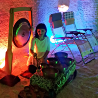 Grota solna, kobieta gra na misach i gongach, w tle 2 leżaki dla uczestników.