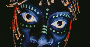 Zdjęcie przedstawia afrykańską maskę, która jest pokryta świecącą farbą.