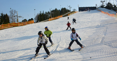 Grupa dzieci zjezdża na nartach na stoku narciarskim nad Maltą.