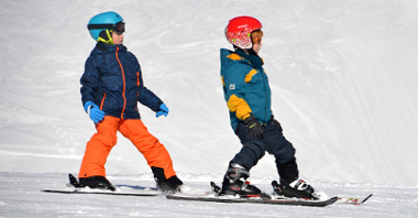 Grupa dzieci zjezdża na nartach na stoku narciarskim nad Maltą.