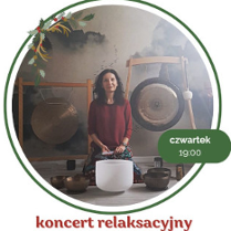 Kobieta w bordowej bluzce siedzi na podłodze. Przed nią stoją misy i gongi do grania.