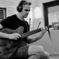 Na zdjęciu mężczyzna w słuchawkach gra na gitarze w studiu nagraniowym
