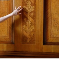 Dłoń na tle drewnianego panelu z intarsją w kształcie dębowych liści.