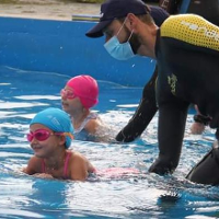 Dzieci pływające w basenie z pomocą asystentów